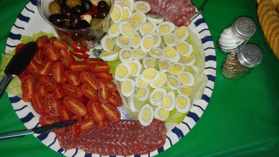 A plate features quail eggs, tomatoes, salami, and olives ready to eat.