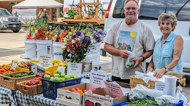 Fisher's Flowers & Produce farmers market vendors standing behind table full of produce at the farmers market