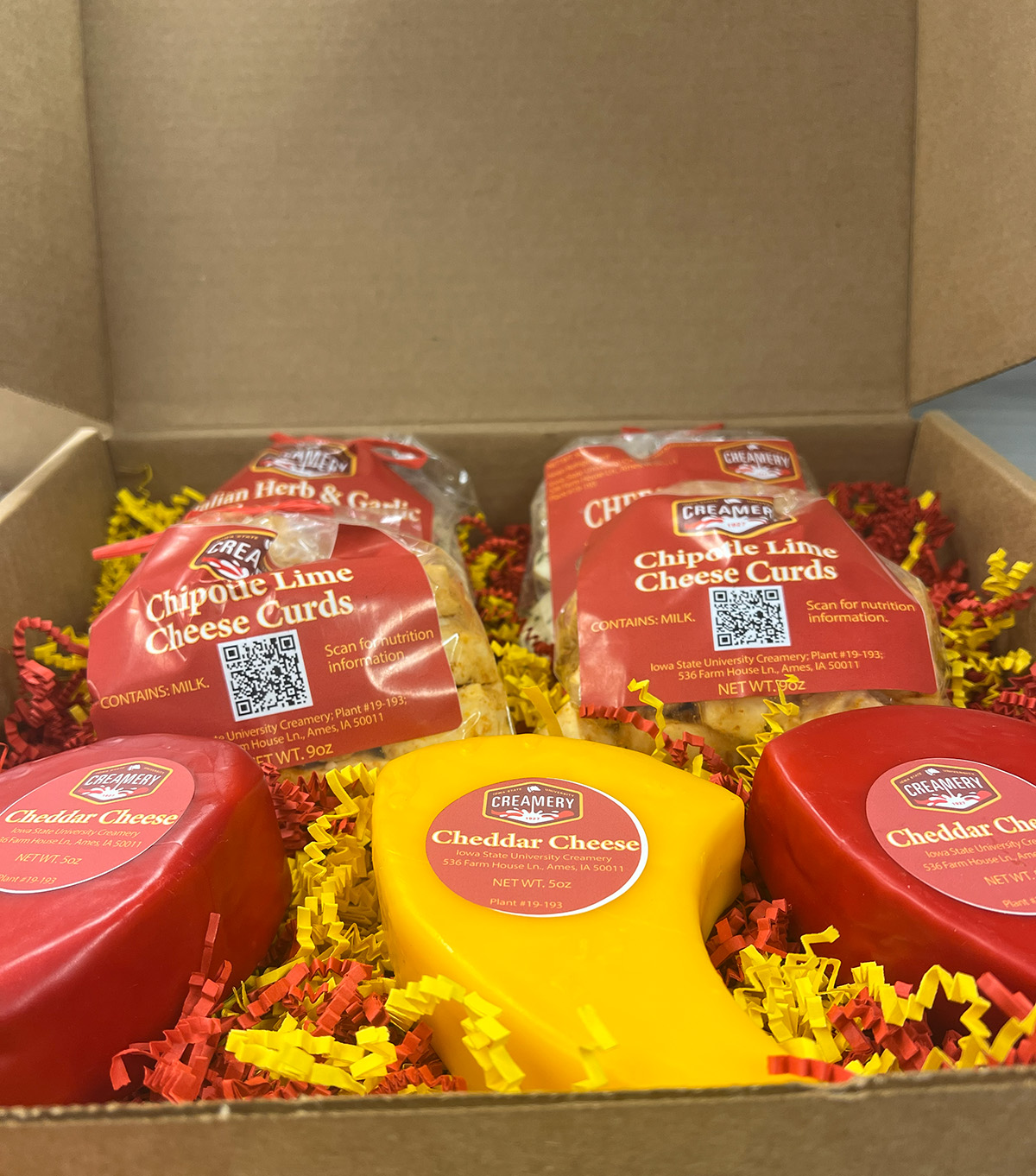 A cheese box from the Iowa State University Creamery is filled with 6 packages of cheese and red and yellow crinkle paper.