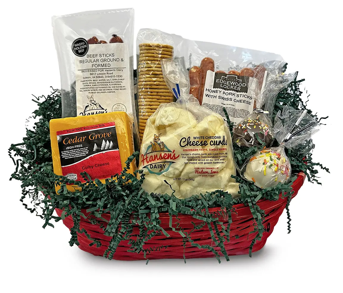 A red basket with green crinkle paper has cheese curds, colby cheese, crackers, a cake pope, and packages of beef sticks.