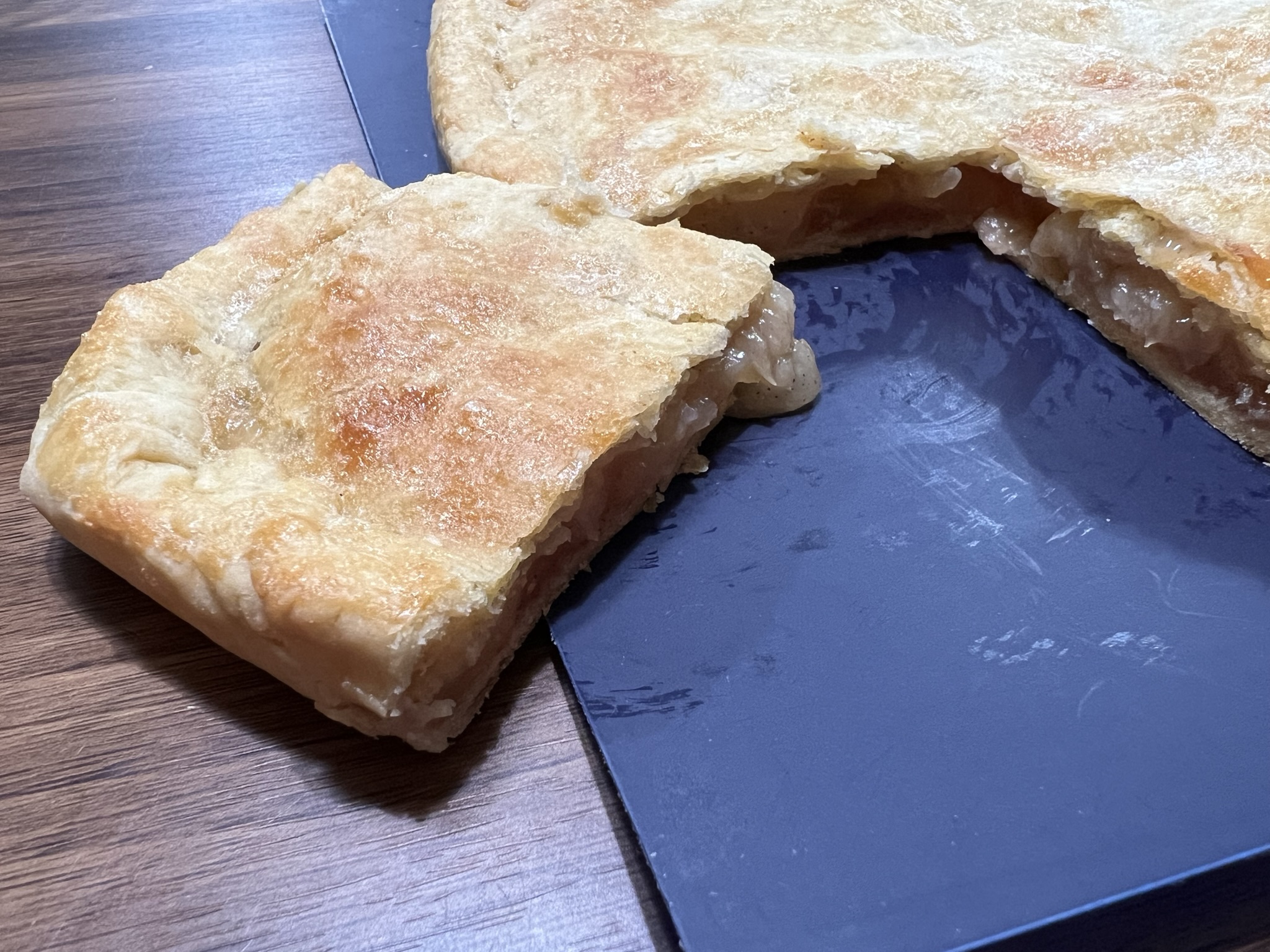 A slice of apple bar sits ready to be eaten next to a tray full of apple bars.