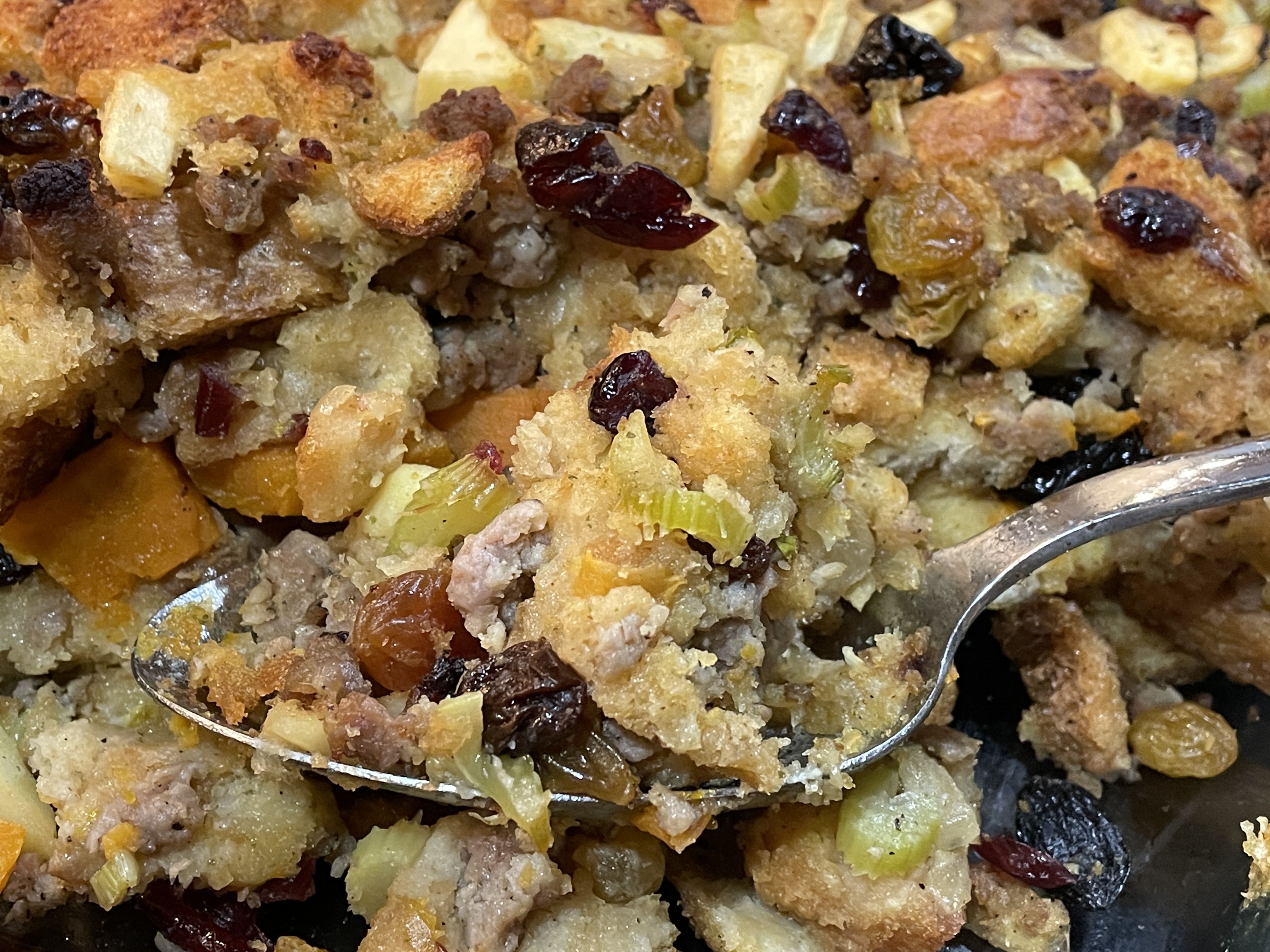 A spoon holds a helping of Savory Sweet Potato and Sausage Dressing