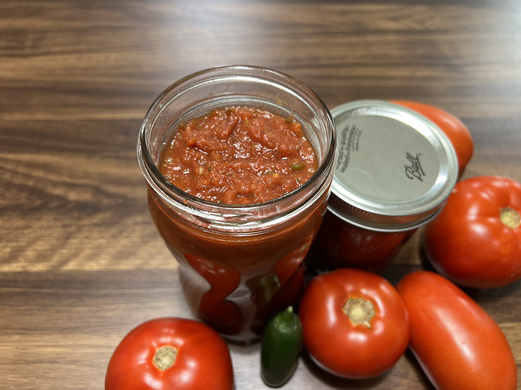 A jar of spaghetti sauce sits ready for a lid.  The jar is surrounded by beautiful tomatoes.