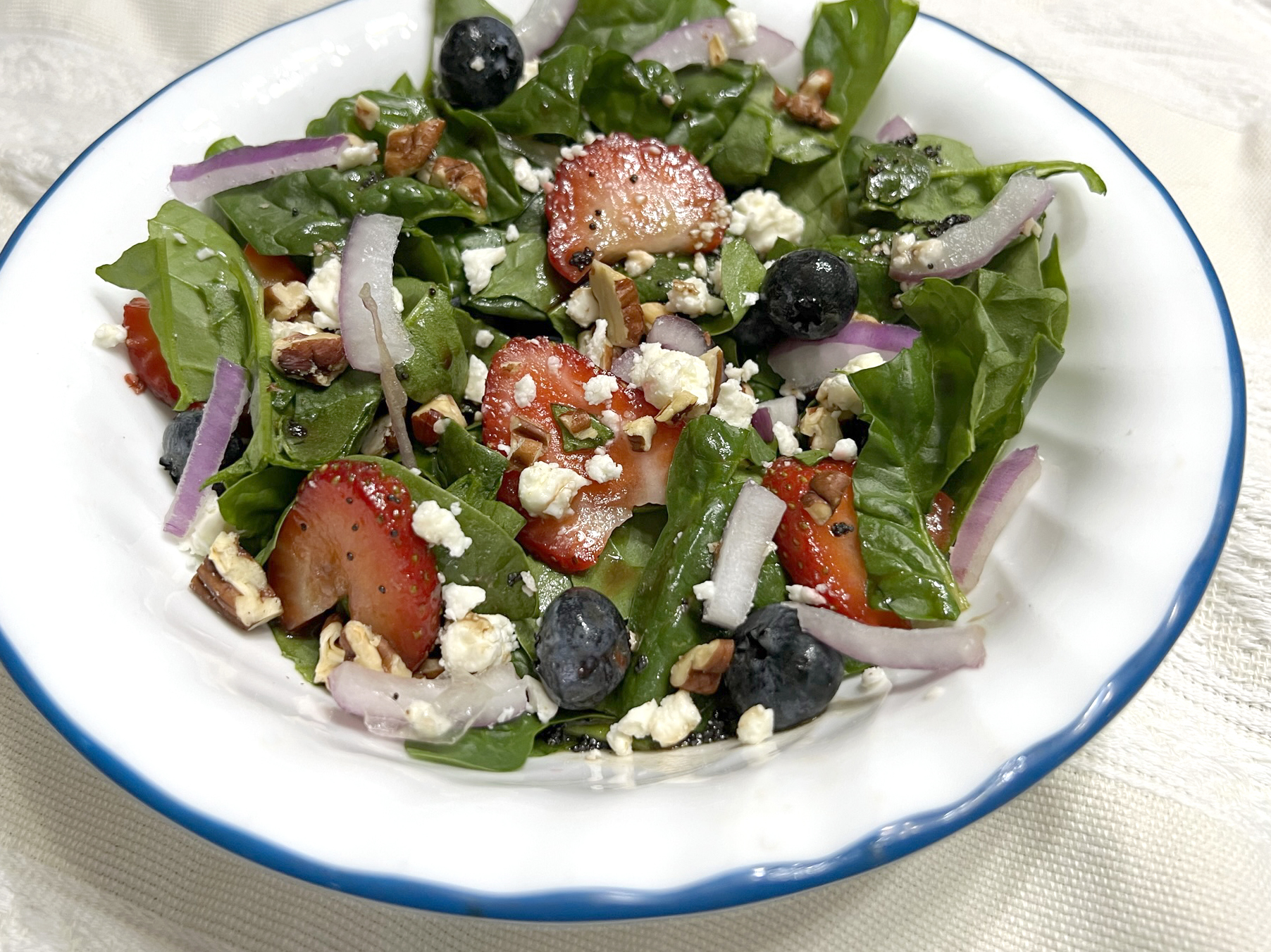 A plate of spinach strawberry salad sits in a white bowl ready to eat.
