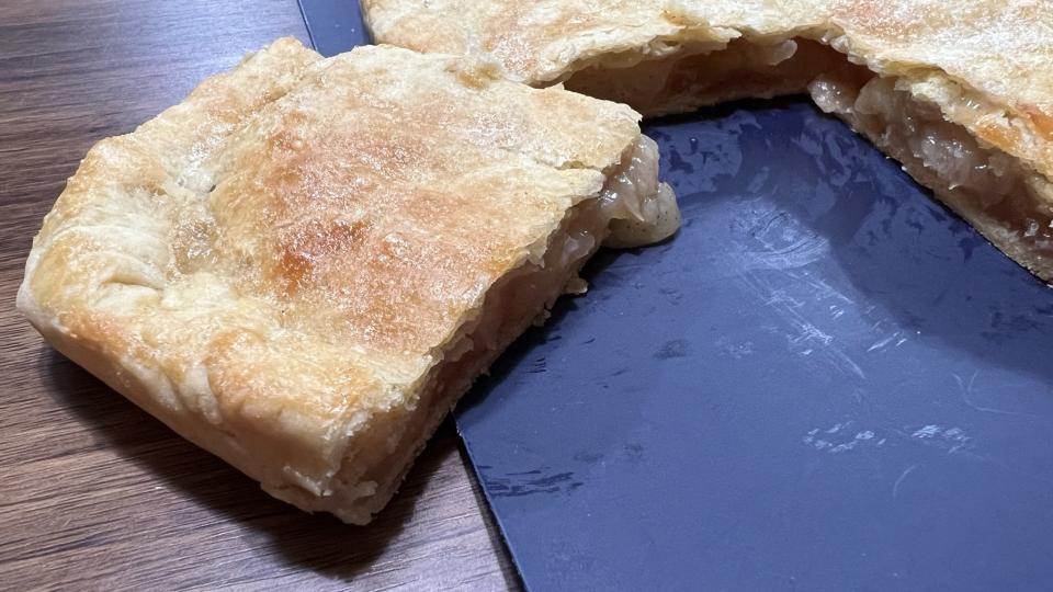 A slice of apple bar sits ready to be eaten next to a tray full of apple bars.