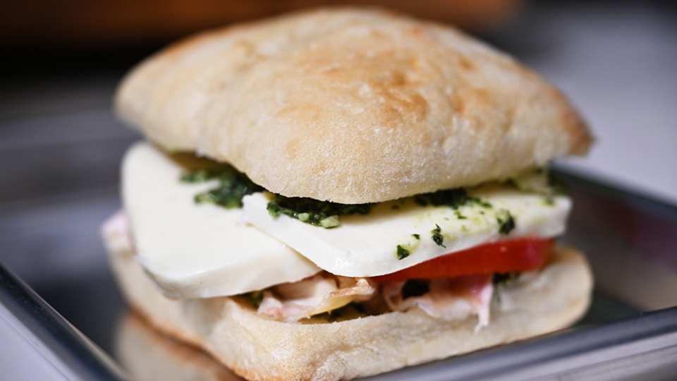 A sandwich made up of a ciabatta role, mozzarella, tomato and pesto sits on a shiny tray.