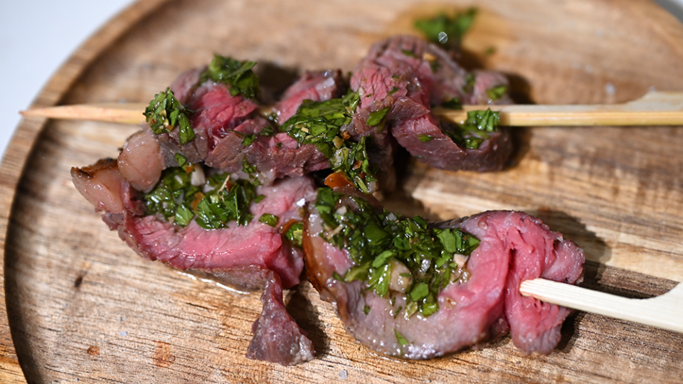 Beef covered in green chimichurri sauce is skewered fresh from the grill.
