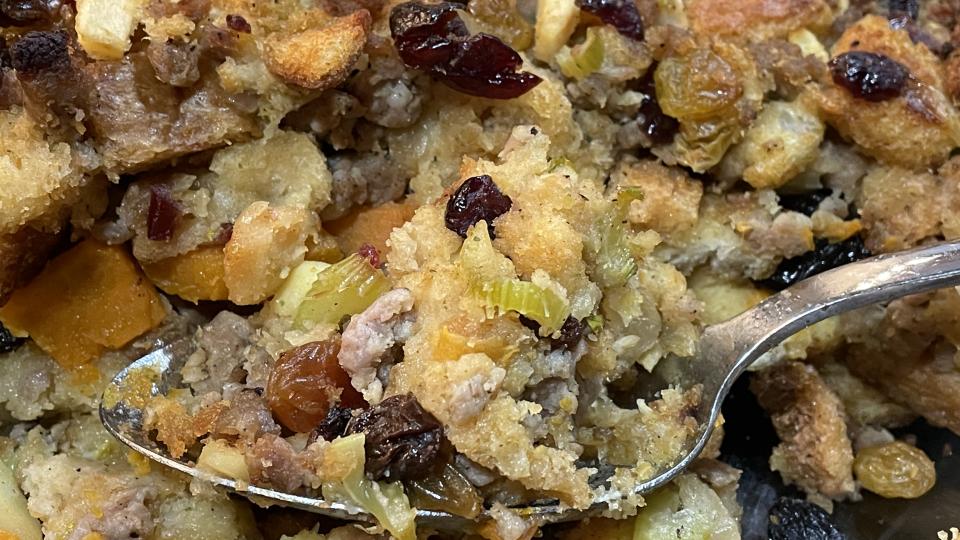 A spoon holds a helping of Savory Sweet Potato and Sausage Dressing