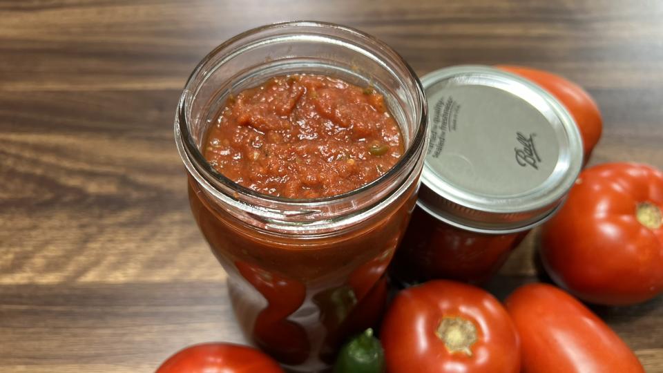 A jar of spaghetti sauce sits ready for a lid.  The jar is surrounded by beautiful tomatoes.