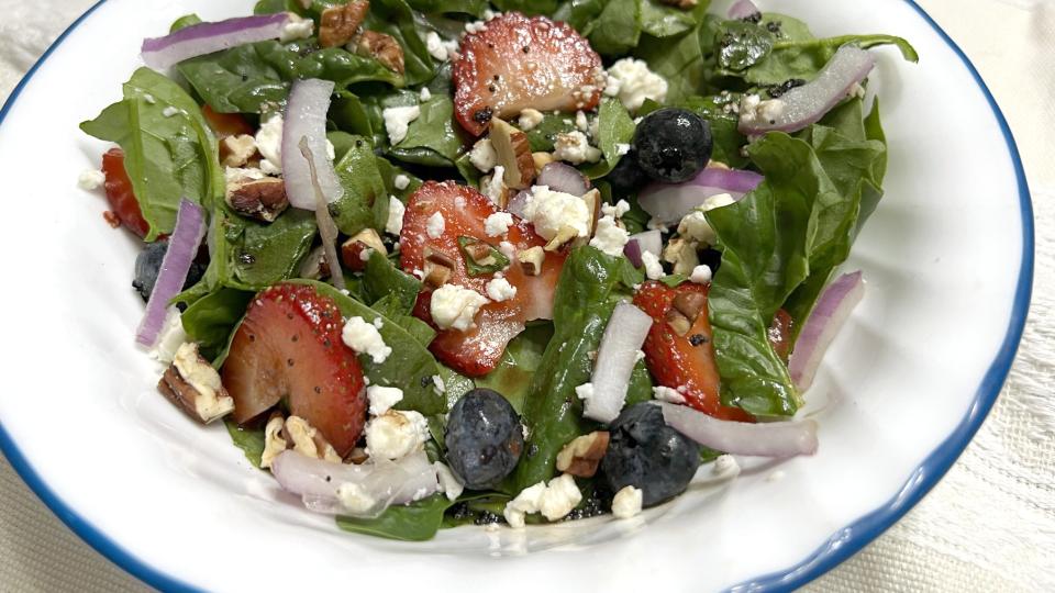 A plate of spinach strawberry salad sits in a white bowl ready to eat.