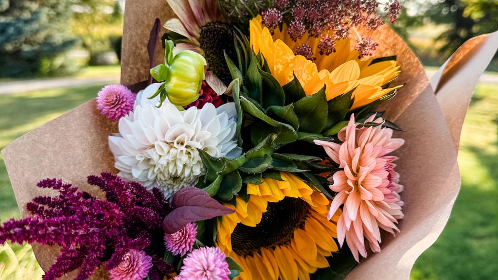 Colorful bouquet of fresh flowers, including sunflowers and dahlias, wrapped in brown kraft paper. 