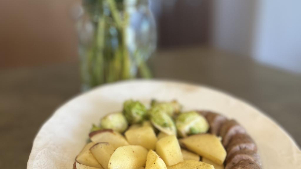 Farm to table meal with brat, potatoes, and brussel sprouts.  Fall flowers in the background.