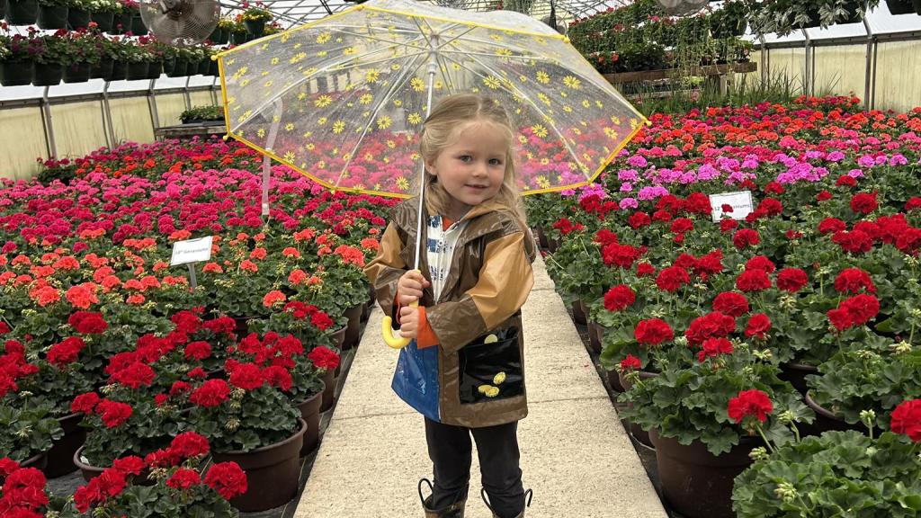 Gehling daughter with umbrella inside family greenhouse with blooming flowers behind