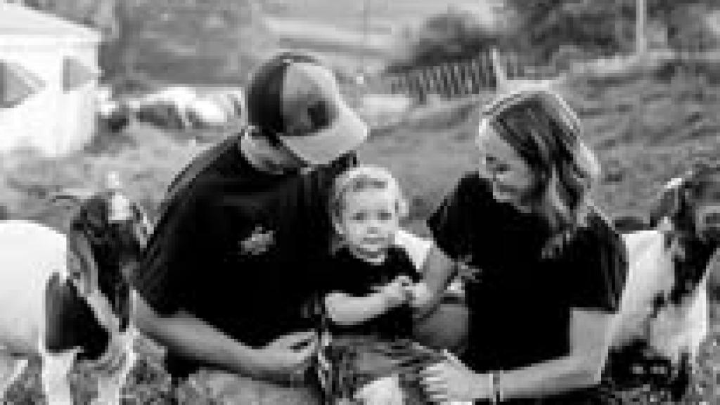 Black and white photo of ReEvolution Farm founders Korrin and Sean with their child and a couple goats