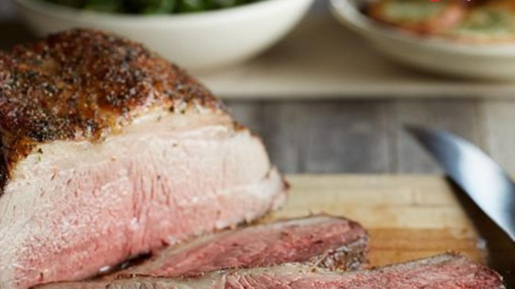 Beef top round roast with slices laying on cutting board and bowl of green cooked vegetables in background