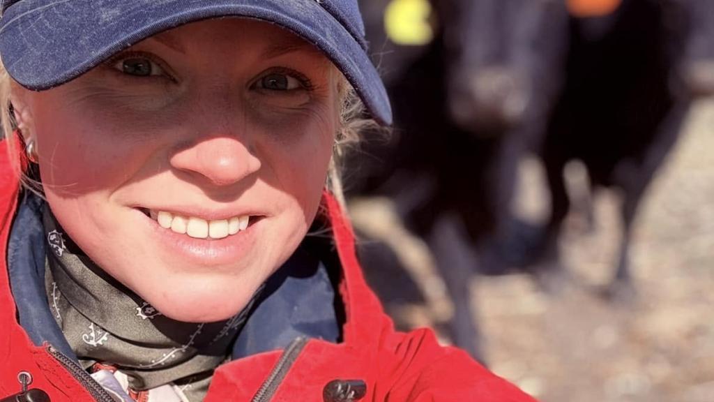 Cora wearing a red coat and cap taking a selfie with black cattle in the background.